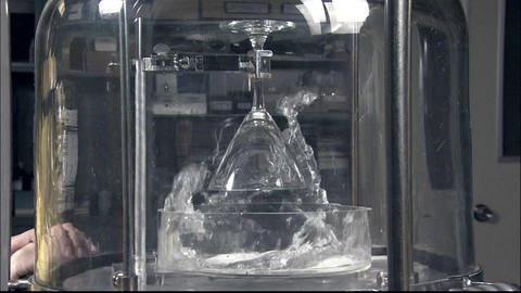 Ein Glas hängt kopfüber in einer Glasglocke, einer Vakuumpumpe. 