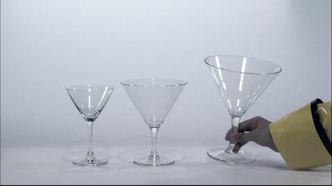 Eine Hand stellt drei Gläser der Größe nach geordnet auf einen Tisch.