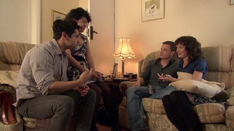 Vier junge Erwachsene sitzen im Wohnzimmer und reden miteinander.