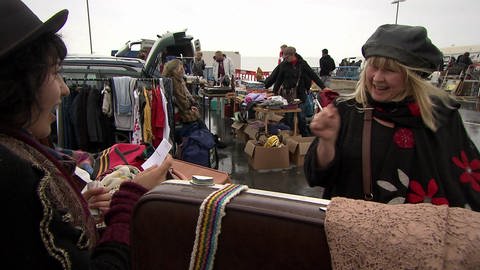 Zwei Frauen stehen auf einem Flohmarkt und unterhalten sich.
