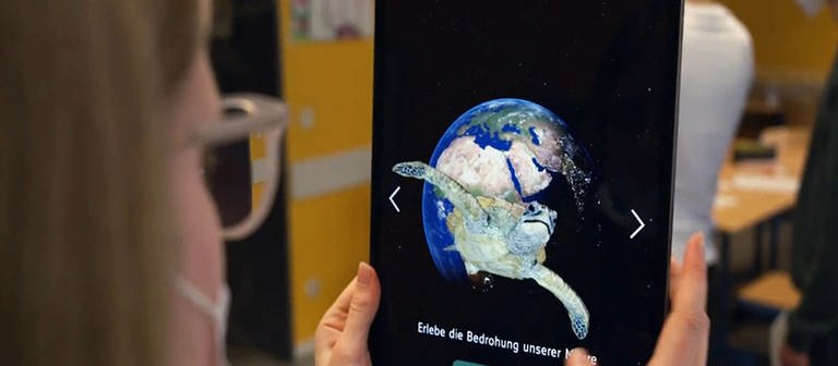 Eine Schülerin nutzt die WDR Klima-App auf einem Tablet, das eine Weltkugel und eine Schildkröte zeigt