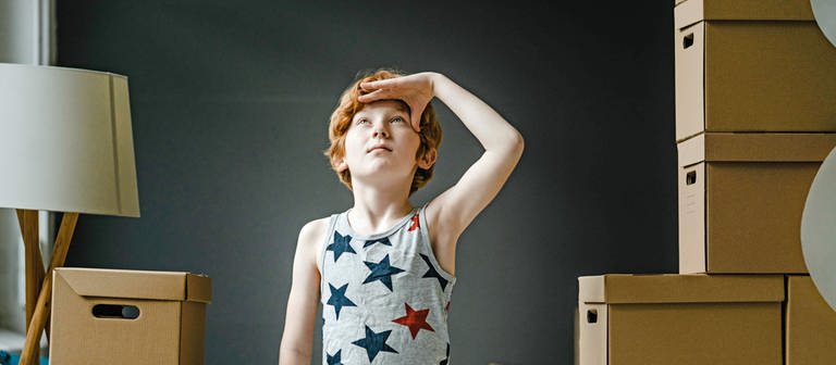 Junge mit Umzugskartons schaut in die Ferne, Umzug Planet Schule