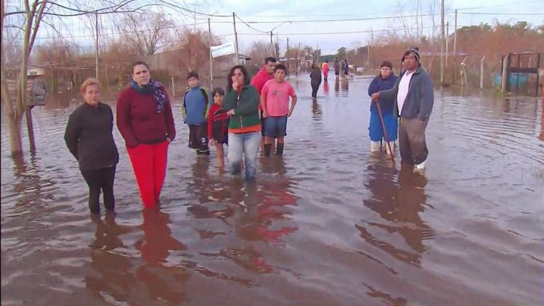 Mehrere Menschen stehen in einer überfluteten Straße.