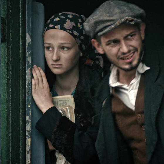 Die Darsteller von Eva und Tomasz schauen aus einer Zugtür.