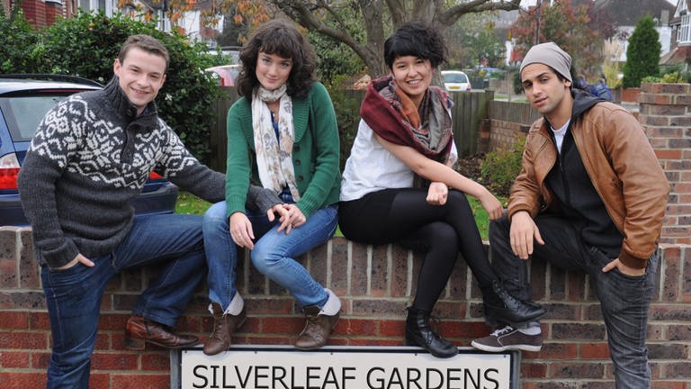 Vier junge Menschen sitzen auf einer Mauer über dem Schild "Silverleaf Gardens".