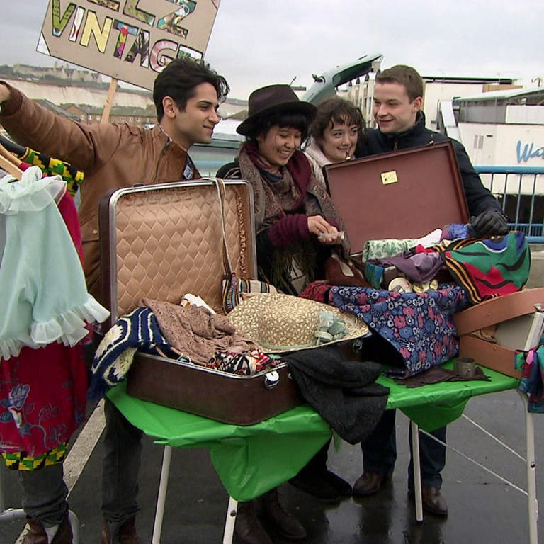 Vier junge Leute stehen an einem Stand auf dem Flohmarkt, vor ihnen viele Kleidungsstücke. (Foto: WDR/ Footstep production)