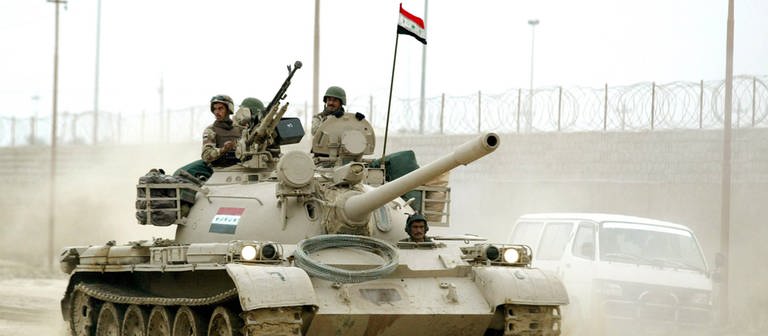 Ein Panzer fährt durch eine staubige Straße in Bagdad, zwei Soldaten schauen hinaus. Internationale Krisen.