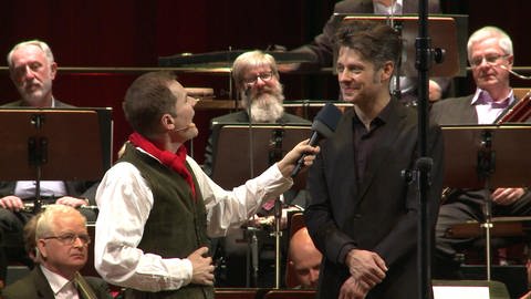 Moderator Malte Arkona interviewt Dirigent Joseph Bastian.