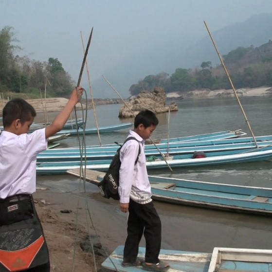 Zwei Jungen in Schuluniform steigen in ein flaches Boot.