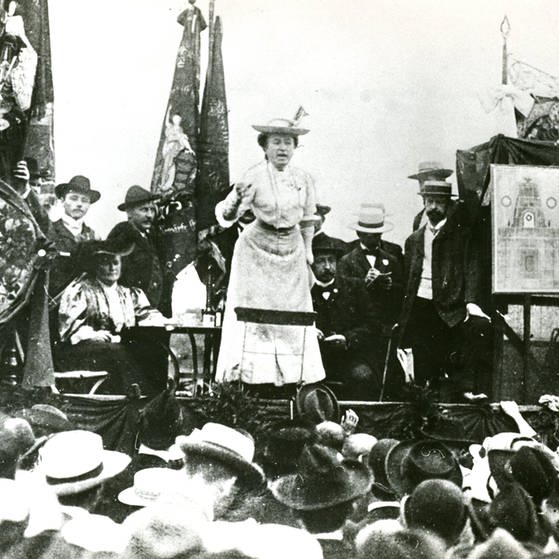 Rosa Luxemburg, die auf einer Bühne steht und redet.