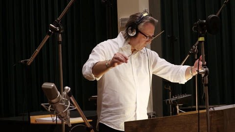 Laurent Eyquem mit Kopfhörer und Dirigentenstab im Studio.