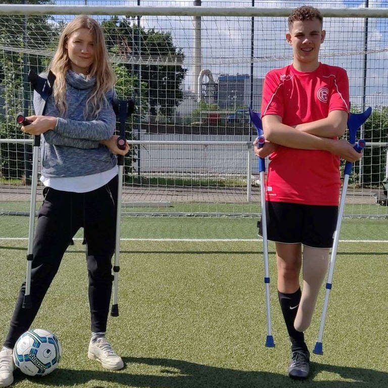 neuneinhalb-Reporterin Jana und der 14-Jährige Jamie stehen mit Krücken in den Händen vor einem Fußballtor. Jamie ist Amputierten-Fußballer, ihm fehlt ein Bein. (Foto: WDR, tvision)