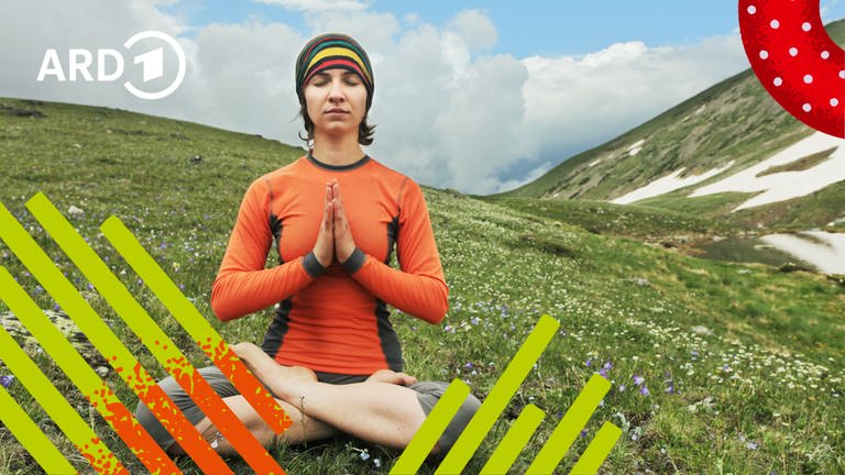 Eine Frau sitzt im Schneidersitz mit geschlossenen Augen und gefalteten Händen vor der Brust auf einem Berg und meditiert.
