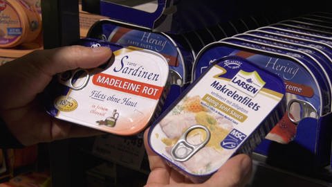 Supermarktkunde hält zwei verschiedene Dosen Fisch in den Händen - eine mit und eine ohne MSC-Siegel.