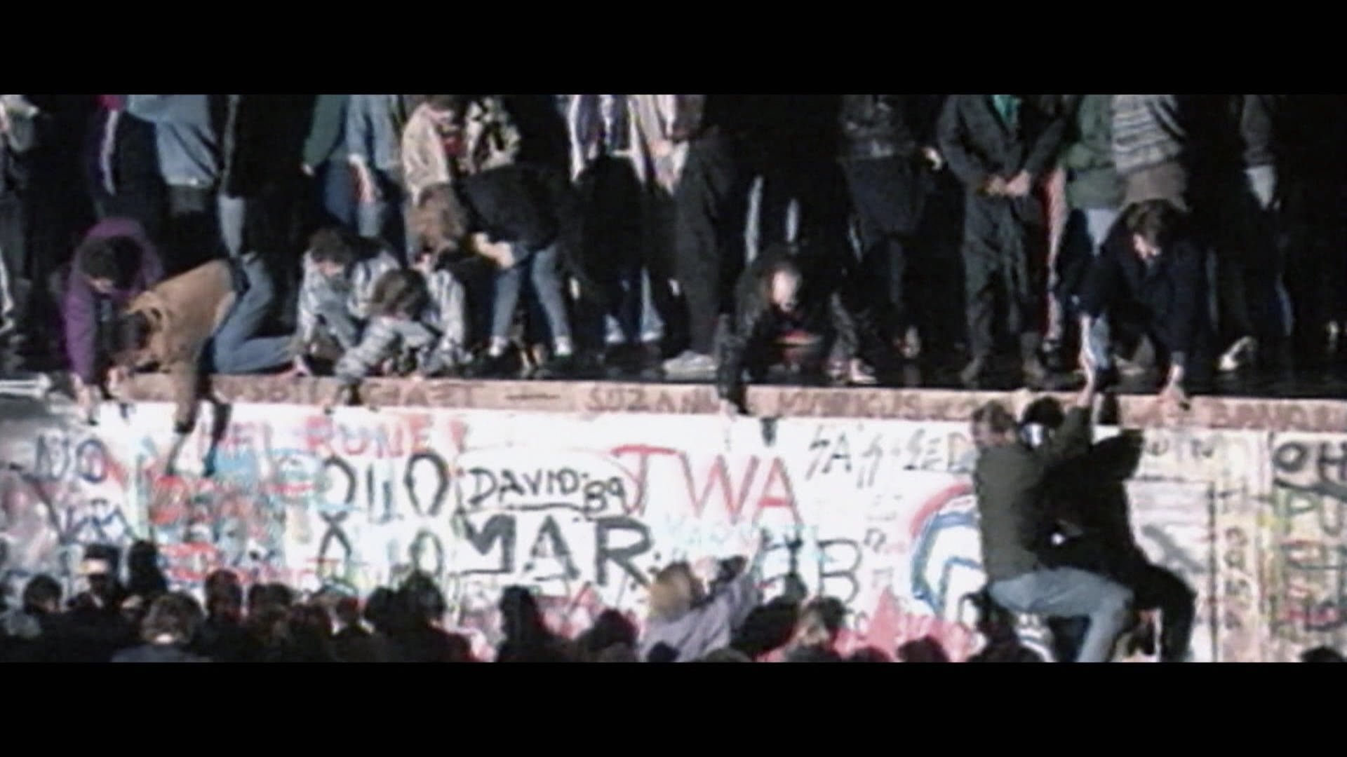 Aufnahme, die viele Menschen auf der Berliner Mauer 1989 zeigt.