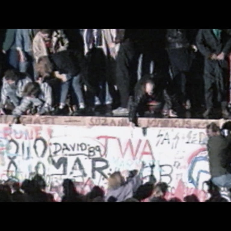 Aufnahme, die viele Menschen auf der Berliner Mauer 1989 zeigt.