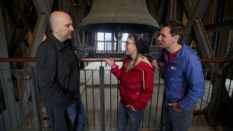 Drei Menschen stehen im Glockenturm des Kölner Dom und sprechen miteinander.