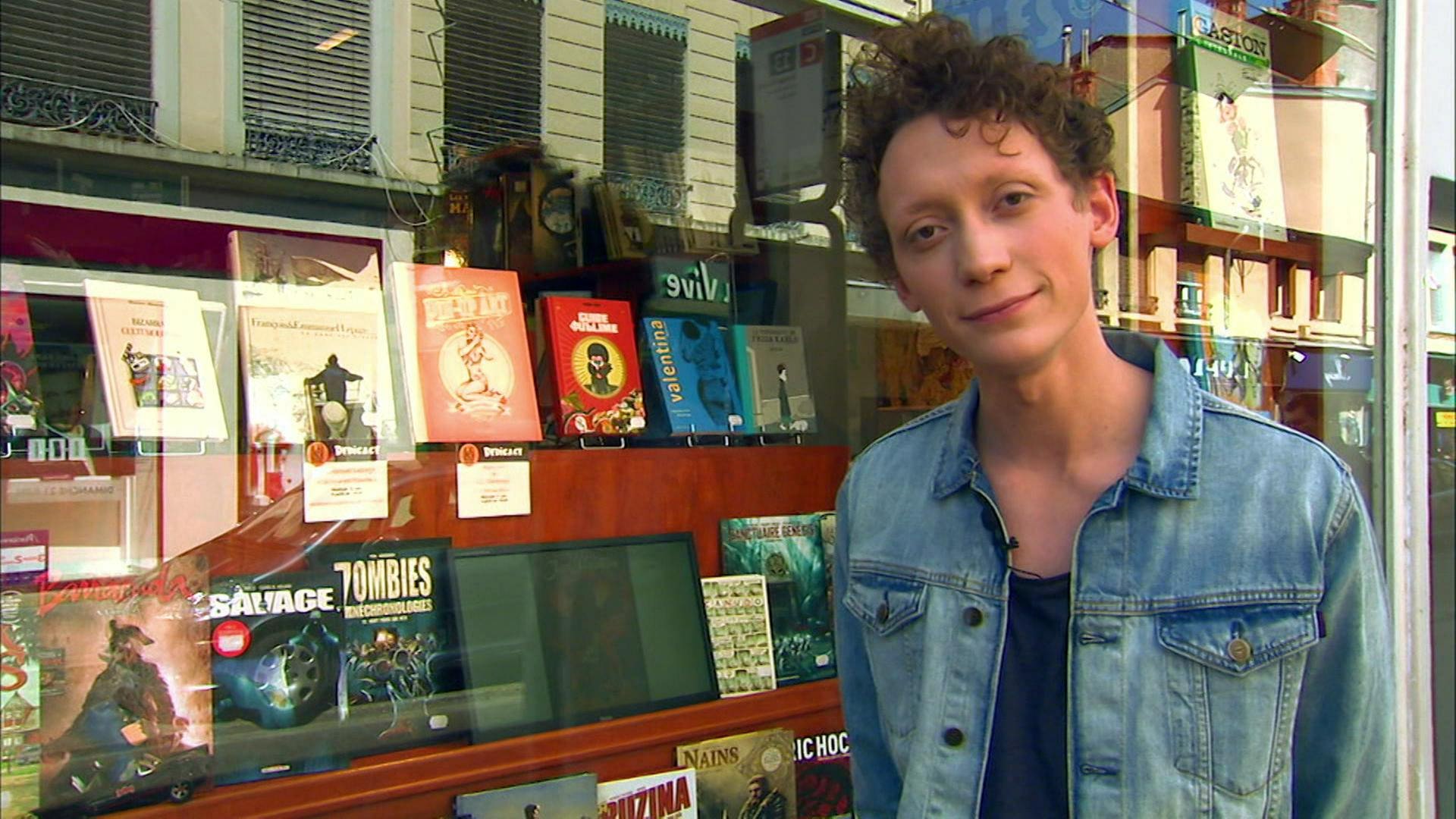 Ein junger Mann steht vor einem Schaufenster voller Comicbände.