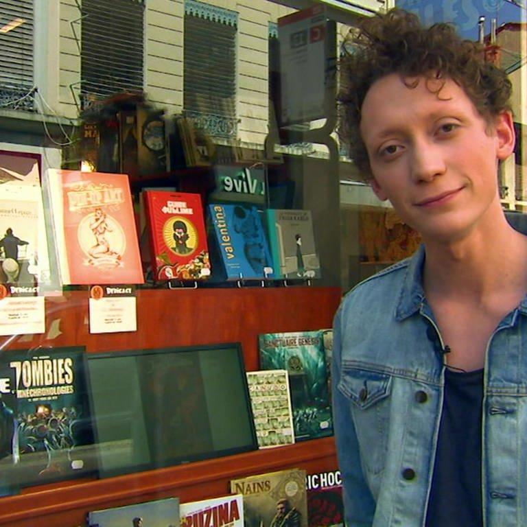 Ein junger Mann steht vor einem Schaufenster voller Comicbände. (Foto: WDR - Screenshot aus der Sendung)