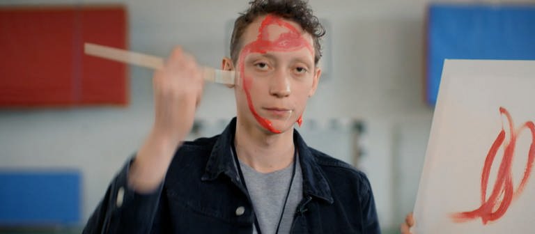 Ein junger Mann bemalt sein Gesicht mit roter Wasserfarbe.