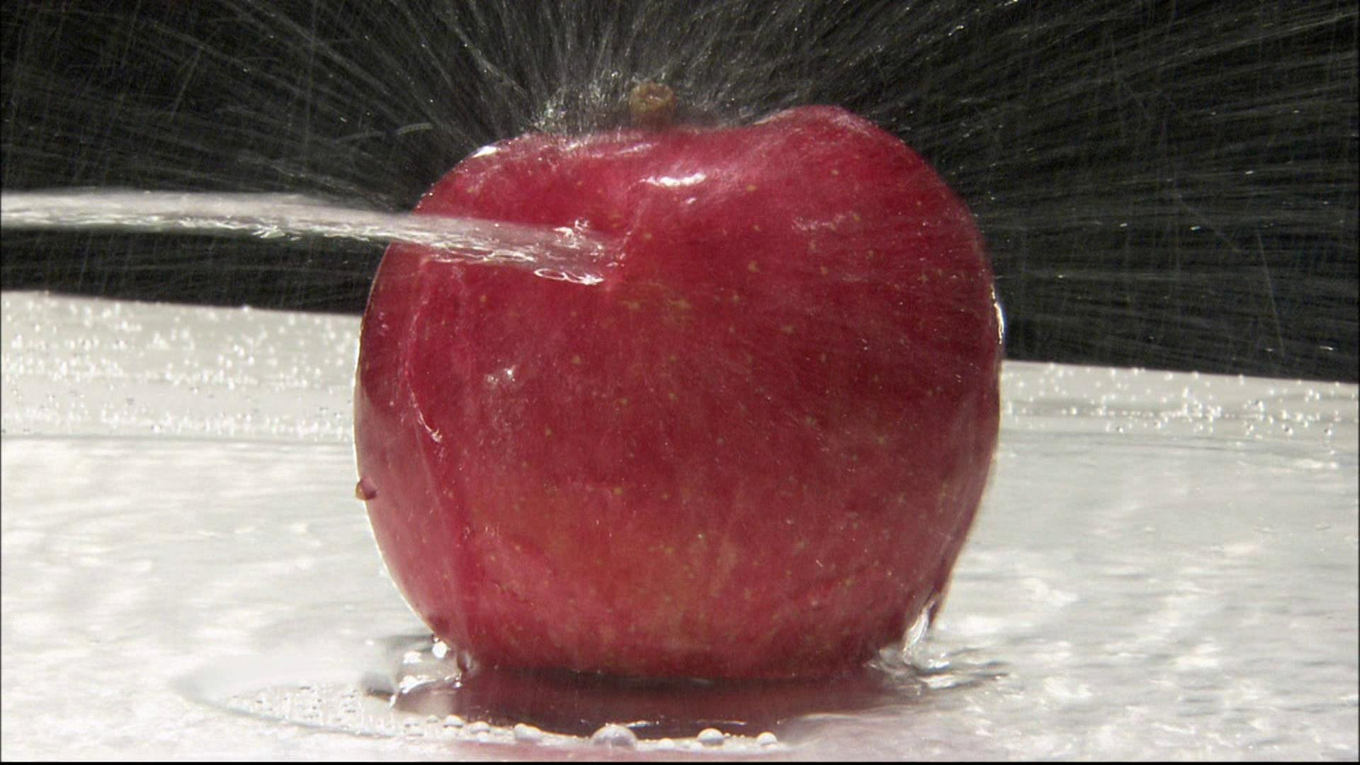 Ein Wasserstrahl trifft auf einen Apfel.