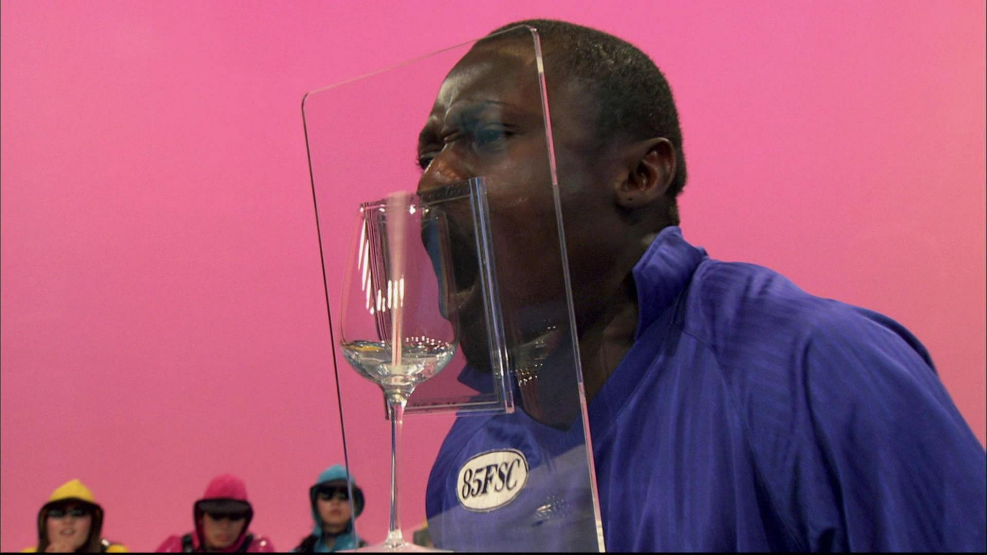 Ein Mann steht vor einer Glasscheib und singt, hinter der Scheibe steht ein Weinglas.