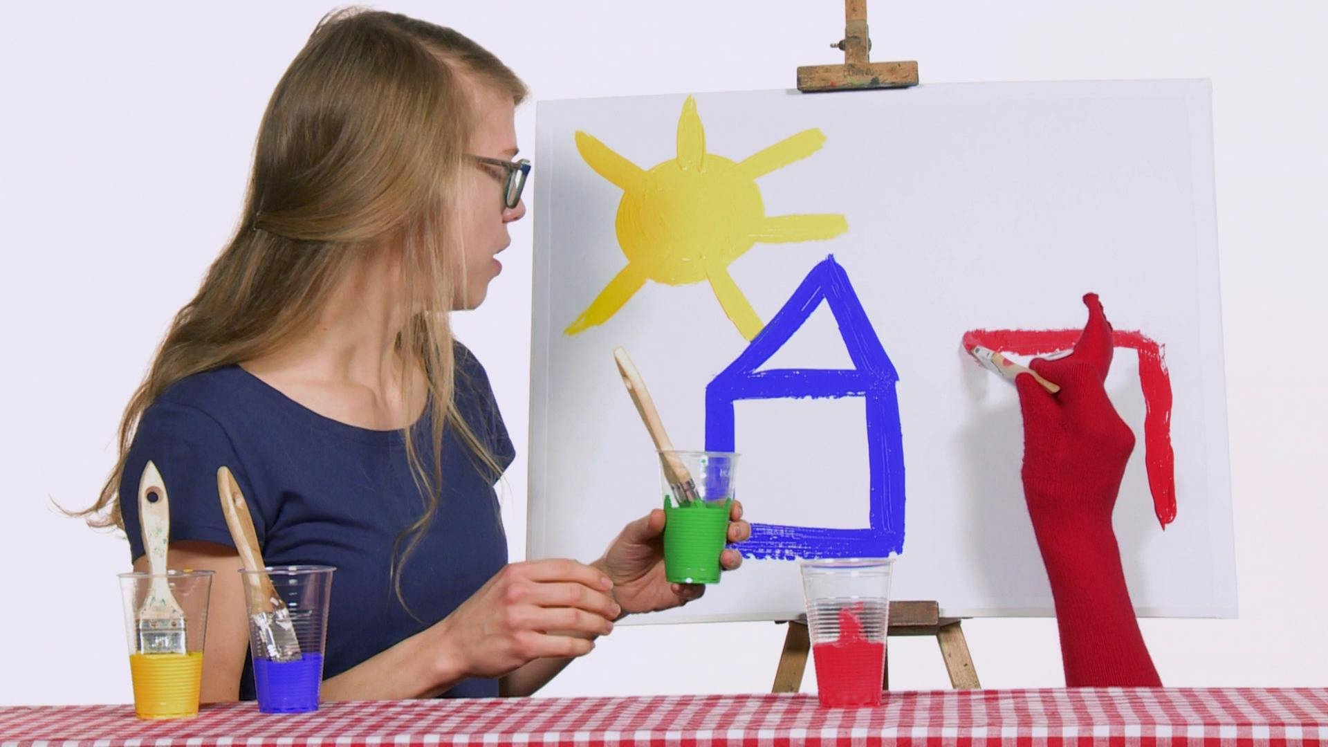 Esther und Socke malen gemeinsam ein Bild. Daruf sind ein blaues Haus und eine gelbe Sonne.