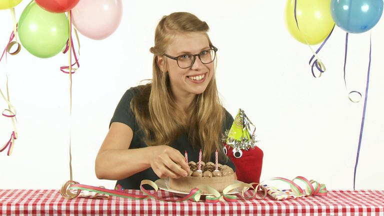 Esther und die rote Socke sitzen an einem Tisch und feiern mit Schokotorte und Luftballons Geburtstag.