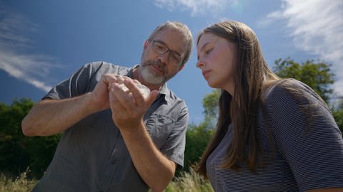 Zwei Forscher stehen neben einem Feld auf einem Blühstreifen und untersuchen eine Probe  (Foto: SWR, Standbild aus der Sendung)