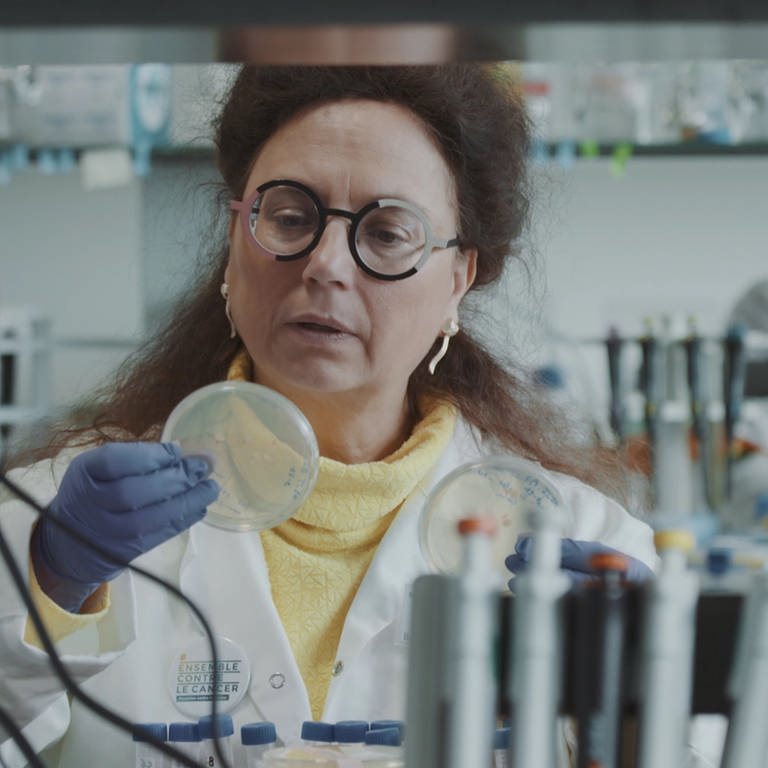 Eine Frau im Laborkittel betrachtet eine Petrischale in ihrer Hand.