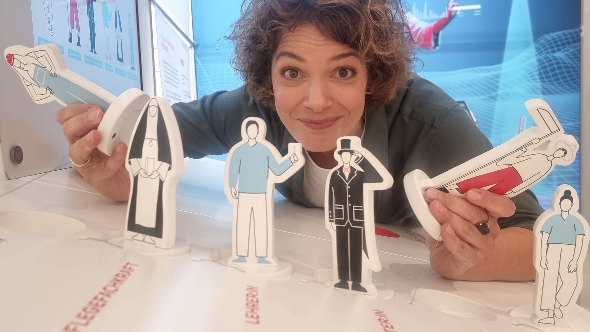 Moderatorin Lena Ganschow mit Pappfiguren, die verschiedene Berufe symbolisieren