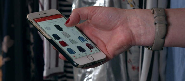 Eine Hand hält ein Smartphone, auf dem Bildschirm sind Kleidungsstücke zu sehen.