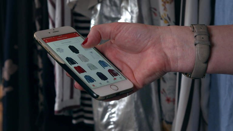 Eine Hand hält ein Smartphone, auf dem Bildschirm sind Kleidungsstücke zu sehen.