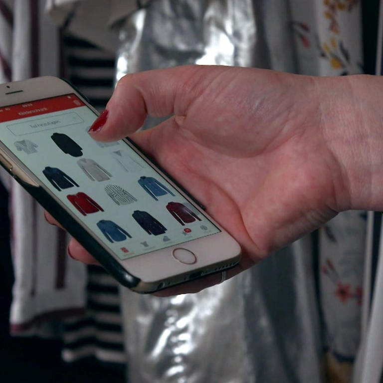 Eine Hand hält ein Smartphone, auf dem Bildschirm sind Kleidungsstücke zu sehen. (Foto: WDR)