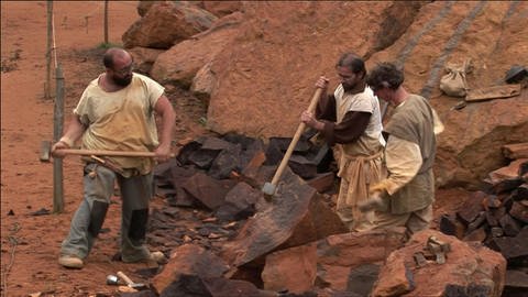 Drei Männer arbeiten mit Hämmern in einem Steinbruch.