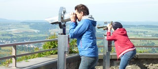 Zwei Leute schauen durch Ferngläser auf eine Landschaft.