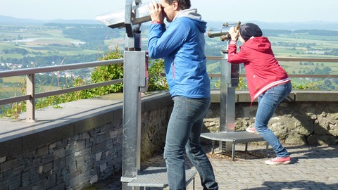 Zwei Leute schauen durch Ferngläser auf eine Landschaft.