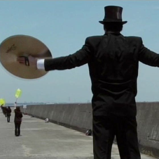 Mann im schwarzen Anzug hält zwei Becken aus Metall in den Händen. (Foto: SWR – Screenshot aus der Sendung)