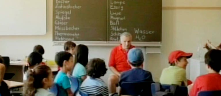 Ein Mann sitzt vor einer Klasse im Klassenzimmer. (Foto: SWR – Screenshot aus der Sendung)