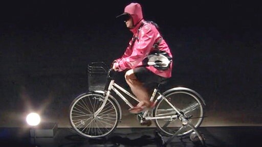 Radfahrer in dunklem Raum, auf dem Boden leuchtet eine Lampe.