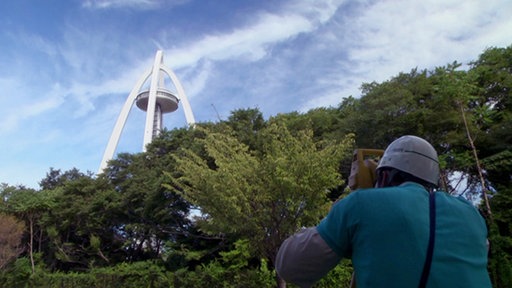 Mann peilt mit Messgerät einen Turm an.