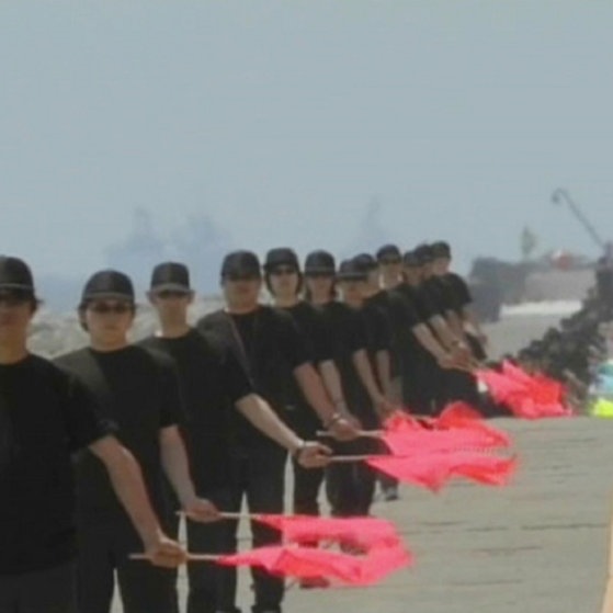 Viele Menschen stehen in einer Reihe auf einer Straße ; jeder hält eine Flagge nach unten gesenkt.