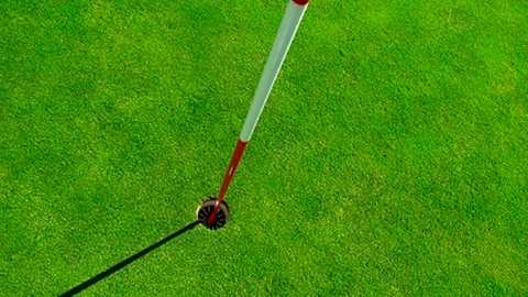 Nahaufnahme eine Golf Lochs, dessen Fahne einen Schatten wirft.