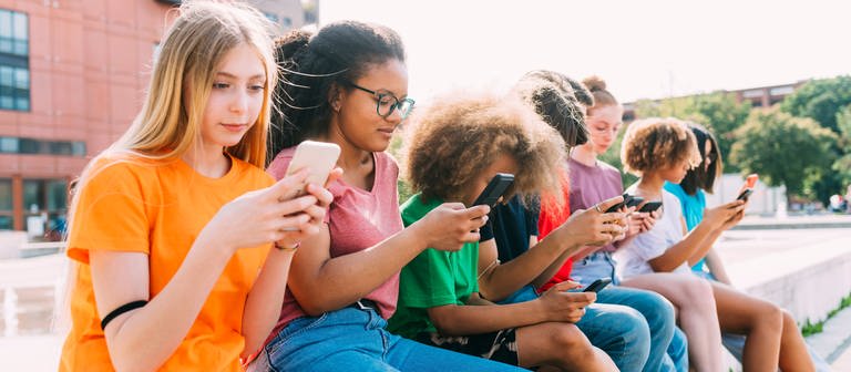 Jugendliche sitzen mit Smartphones auf einer Bank vor der Schule