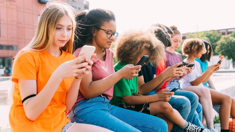 Jugendliche sitzen mit Smartphones auf einer Bank vor der Schule