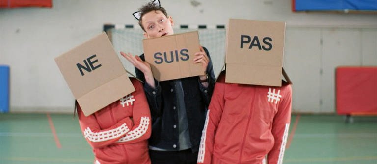 La negation: Moderator Jonas zwischen zwei Personen mit Karton auf dem Kopf, es bildet sich der Ausdruck "ne suis pas" (Foto: WDR)