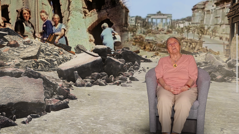 Eine ältere Dame sitzt in einem Sessel - im Hintergrund: Trümmer in Berlin (Screenshot aus der App)
