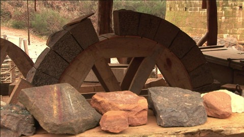 Verschieden geformte Steine auf einem Tisch und einem Holzrad.