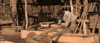 Ein Mann bearbeitet einen kleinen Wagen aus Holz mit einem Ziehmesser.