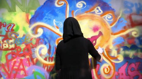 Frau mit schwarzem Kopftuch beim Sprühen eines Graffito. (Foto: SWR - Screenshot aus der Sendung)